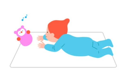 A baby lies on their tummy and looks toward a colorful toy.
