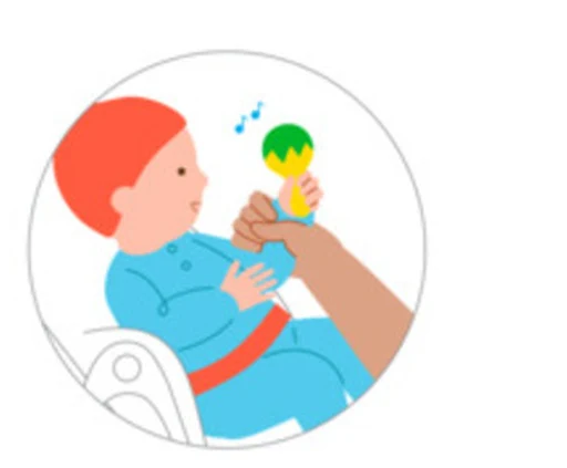 A baby looks closely at a colorful toy while a caregiver stays nearby.