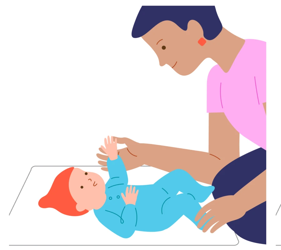 A caregiver sits beside a baby lying on a clear play mat.