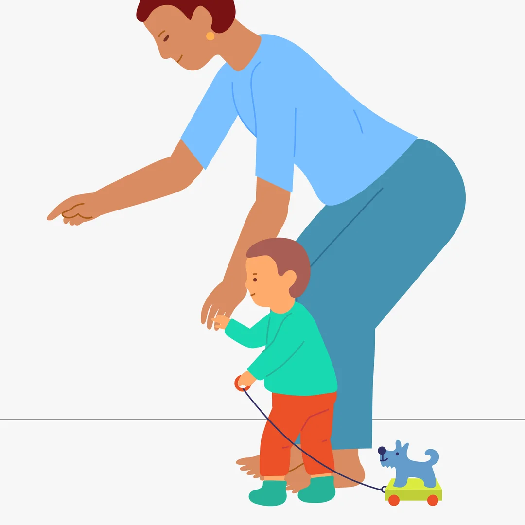 Illustration for “A Walk with the Dog on a String”, step 2: Suggest: “Let’s pull the dog around the room.” Help the child stand up and place the handle in their hand: “Let’s go!” Hold the child’s hand and take a few steps forward.