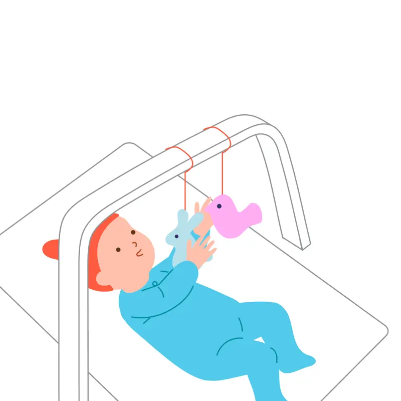 A baby reaches toward two toys attached to a play gym.